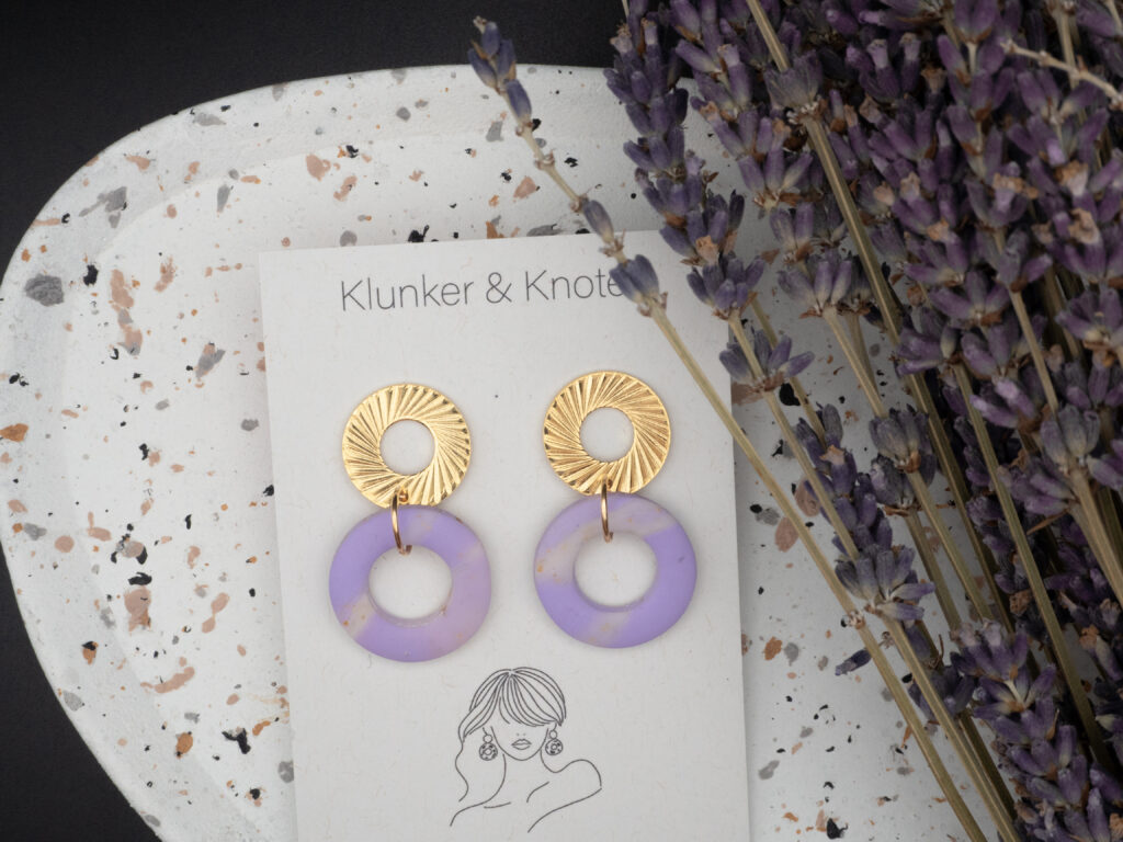 Goldfarbene Ohrringe mit Anhängern in Rund und in lavendelfarben.