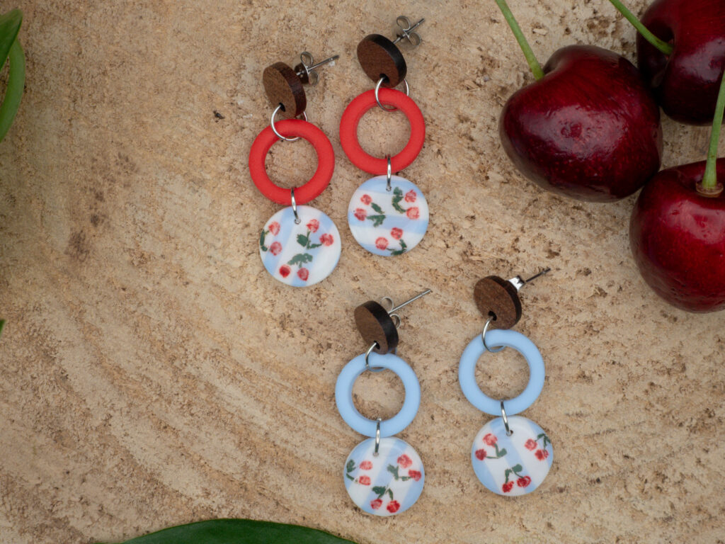 Längliche Ohrringe aus Edelstahl mit runden Anhängern aus Polymer Clay, darunter einer mit handbemalten Kirschen